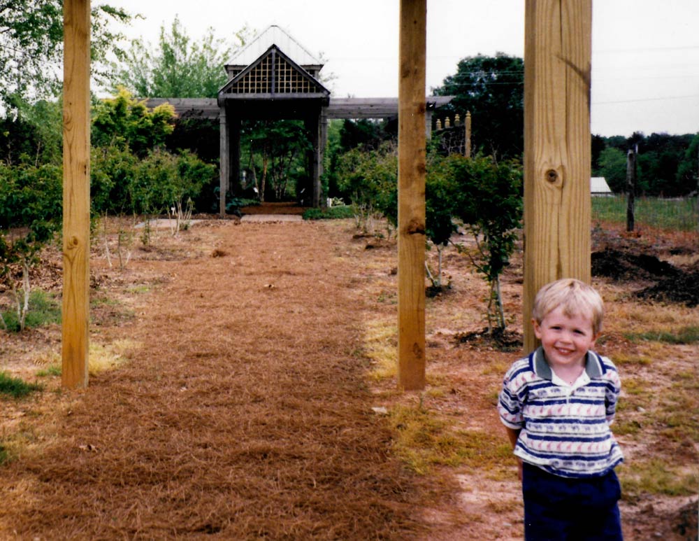 A young Connor Lichtenfelt standing in the nursery’s pergola display garden